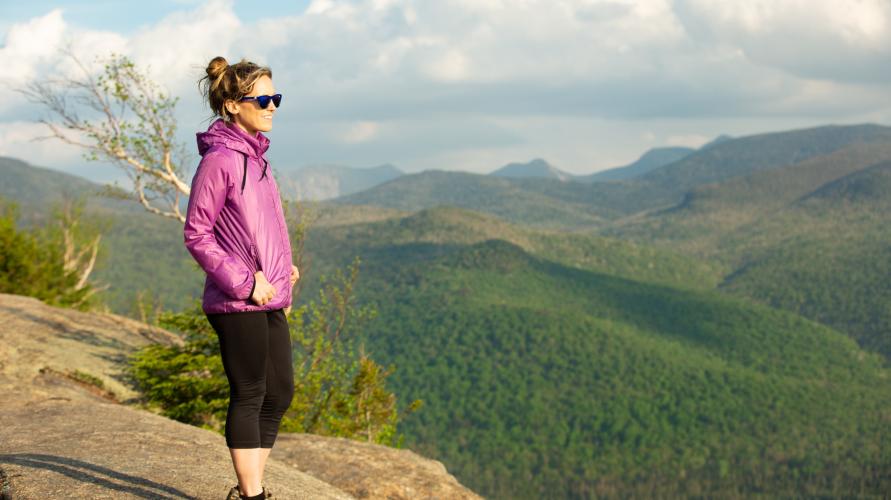 A woman on the summit of a mountain looks out over the Adirondacks