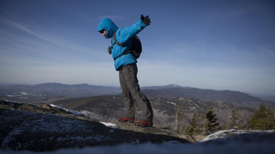 Hiker with open arms stands in front of a summit view