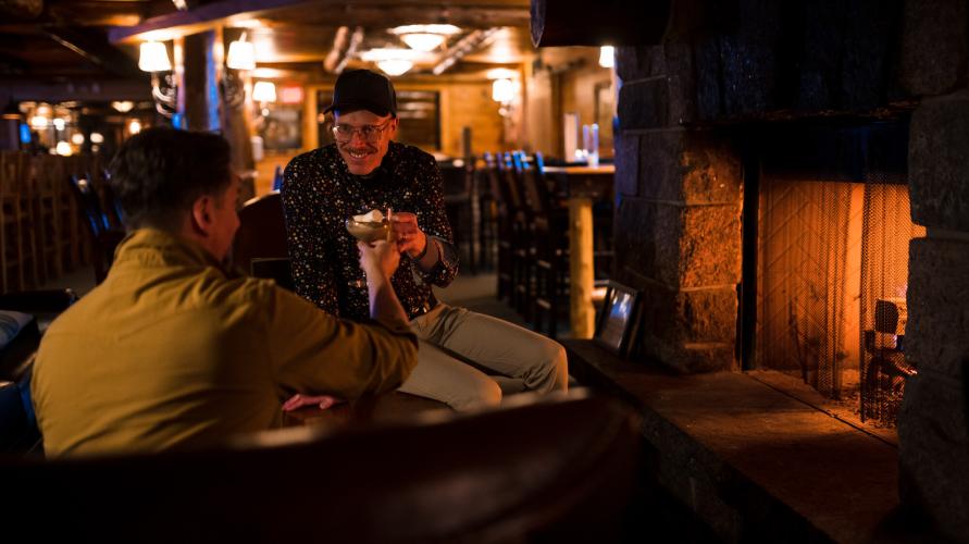 A couple sits next to a fireplace with drinks in their hands.