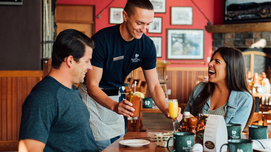 A man and woman are served cocktails at a lodge-style restaurant.