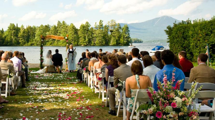 A colorful wedding ceremony in the shade with the high peaks and a lake in the background.