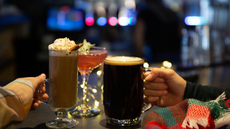 A close-up of two women drinking a dark beer and a spiked hot chocolate. 