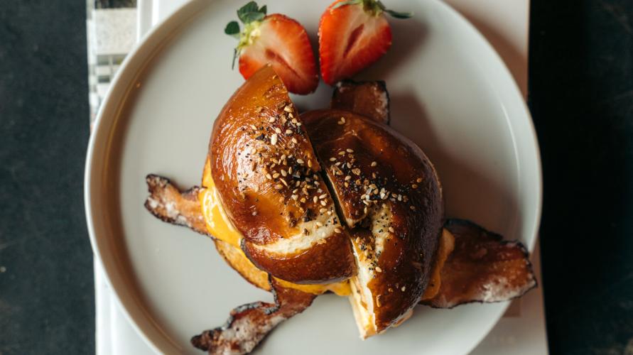 A breakfast sandwich on a toasted bun with strawberries on the side.