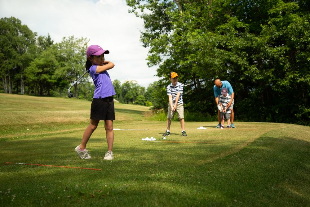 Three children line up to hit golf balls on the green.