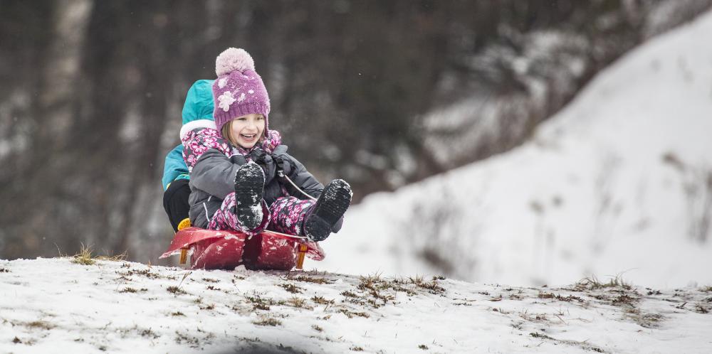 Two small kids smile as they slide down a hill on a plastic sled