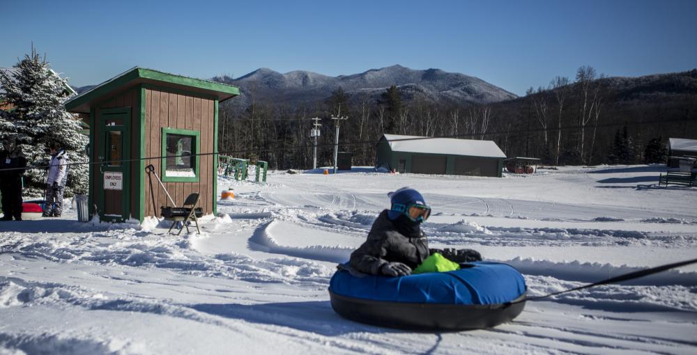 A child sits in a snow tube that is being pulled to the top of a sledding hill by tow rope