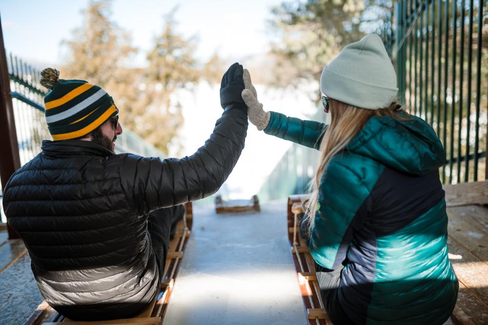 A couple sits on toboggans at the top of the Lake Placid toboggan chute