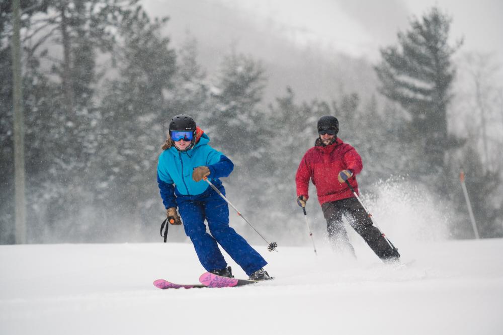 two skiers race down the mountain during snowfall.