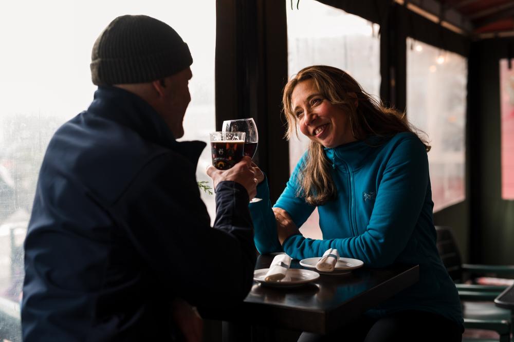 A man and woman cheers wine at a window-side table.