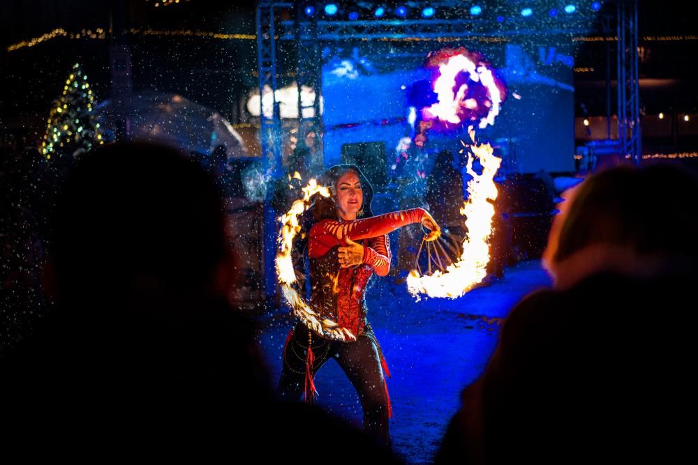 A dancer twirls flaming sticks in front of a crowd at night.
