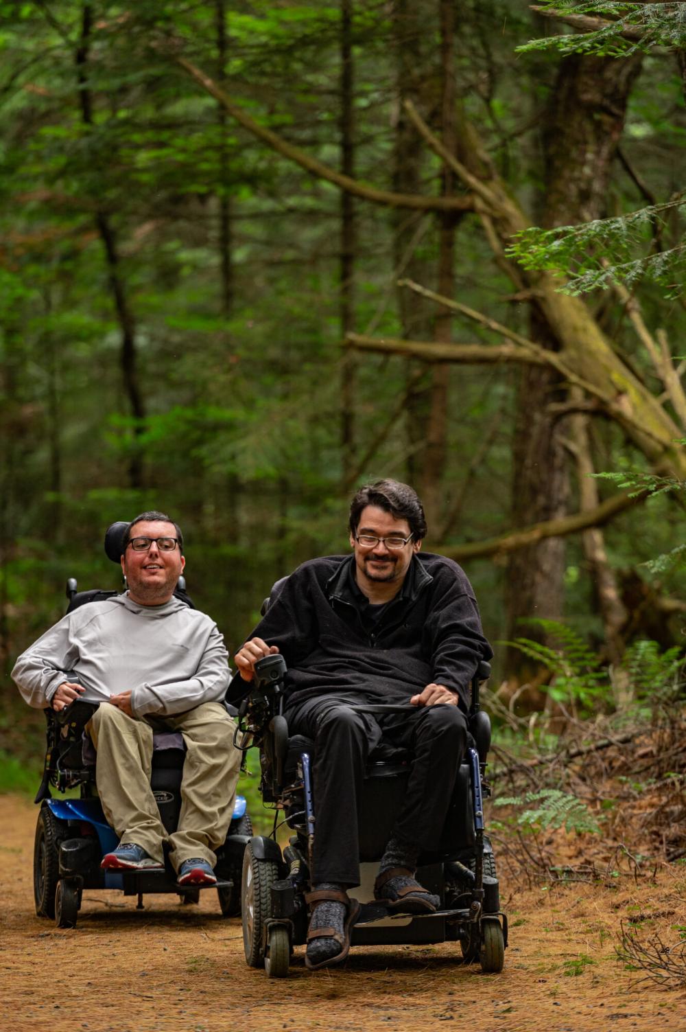 Two men with wheelchairs enjoy exploring a trail through the woods.