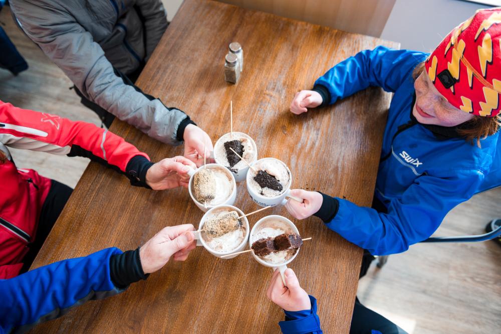 Looking down at a wooden table where a group of people toast with mugs of hot cocoa.