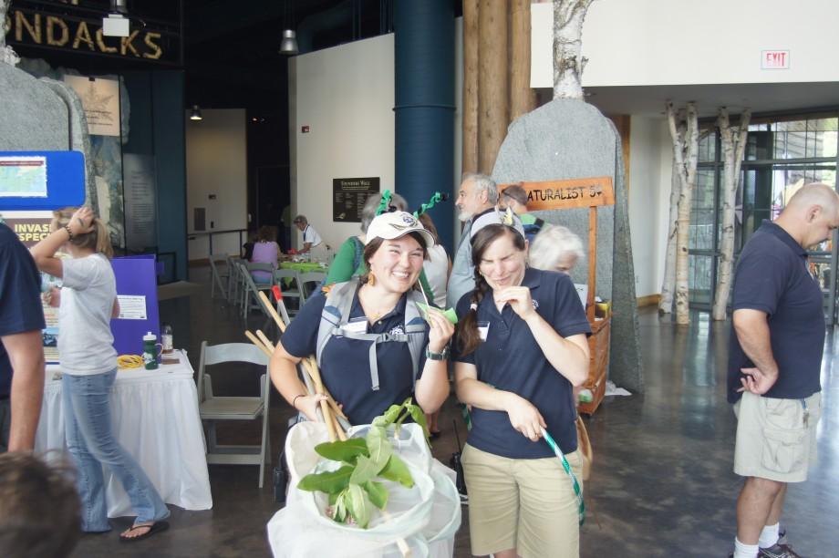 Wild Center naturalist Kendra Ormerod (right) and seasonal naturalist Katie Morgan try eating grasshoppers - with very different reactions! - during BuzzzFest, a Wild Center event centered around insects. Kendra and Katie - Buzzzfest