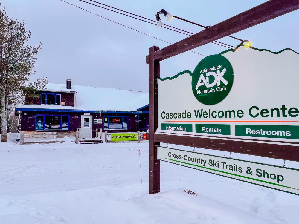 Cascade Welcome Center's sign in front of the snow-covered Adirondack Mountain Club building