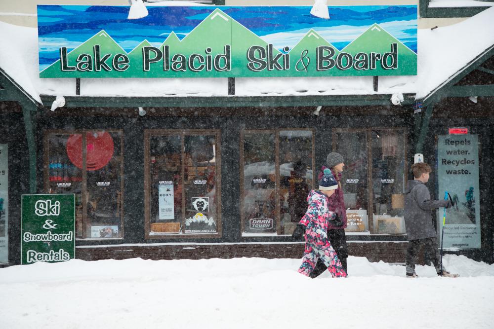 Snow is falling as a family walks by Lake Placid Ski and Board