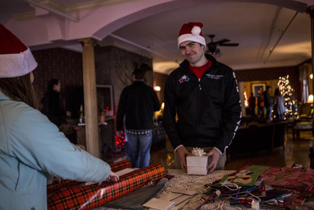 A man in a Santa hat poses at a gift wrapping table.