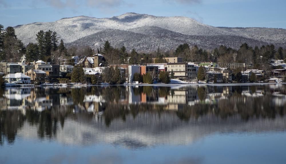 A view across a lake at a snowy village with mountains beyond.