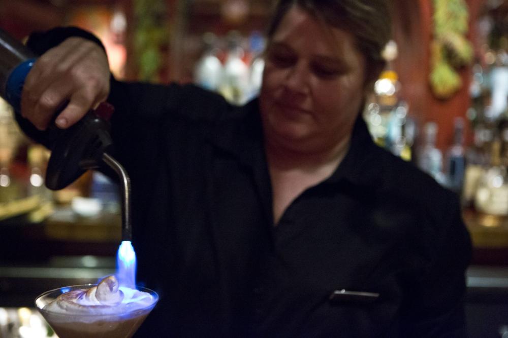 A bartender uses a small torch to brulee a cocktail.