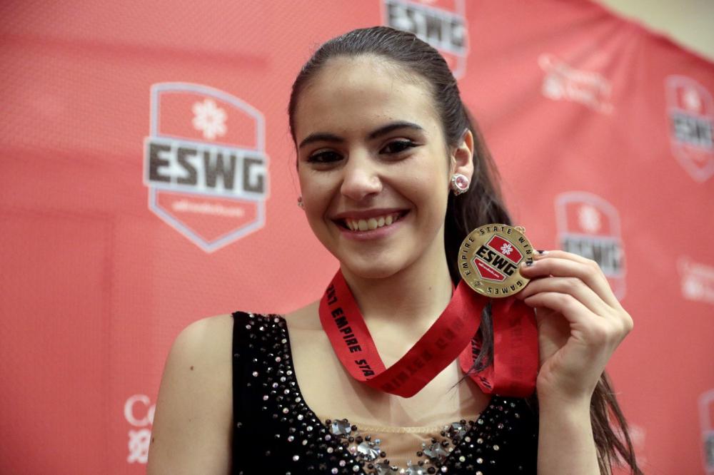 A teenage figure skater smiles and holds up her Empire State Winter Games medal.