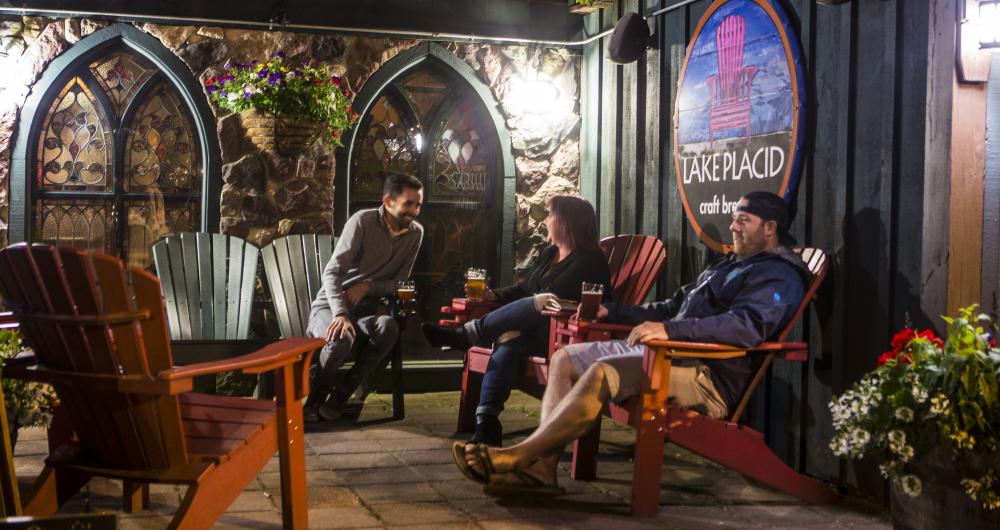 Three people socialize in Adirondack chairs at the Lake Placid Pub & Brewery.