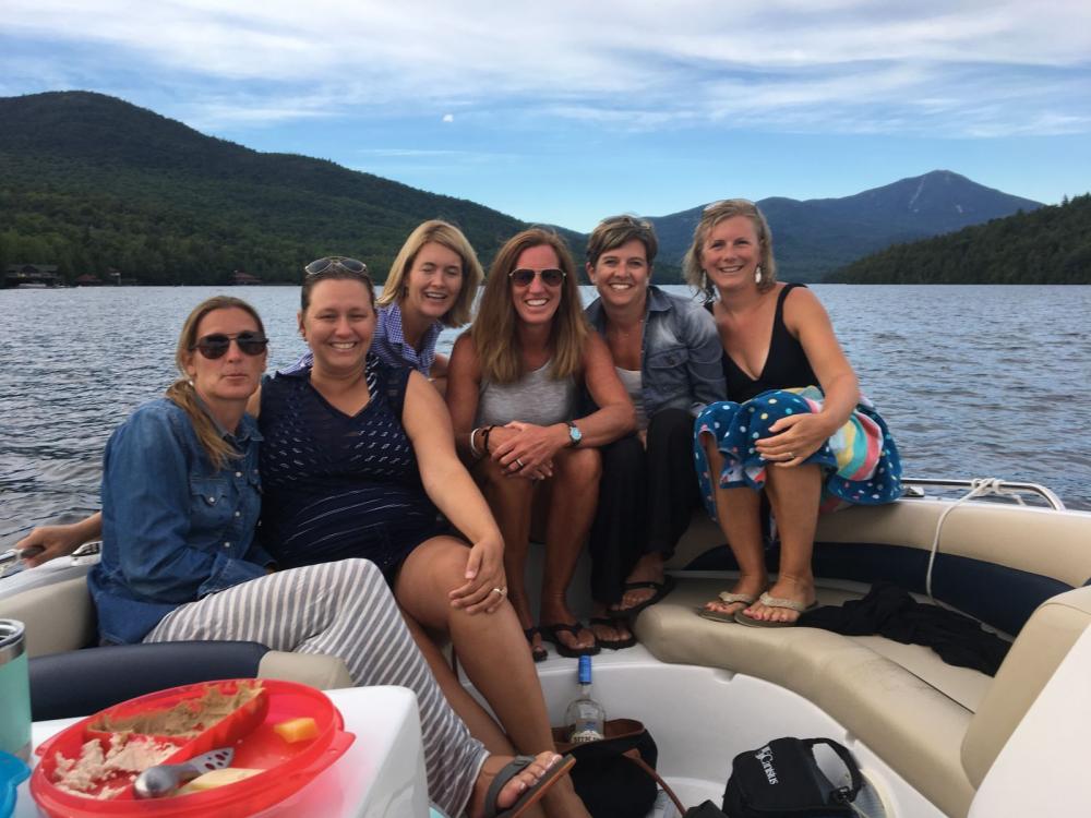 Six women on the front of a boat on one of Lake Placid's boat tours with mountains in the background