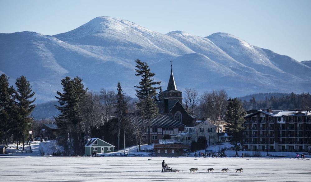 Two people dog sledding in Lake Placid on Mirror Lake with mountains in the background