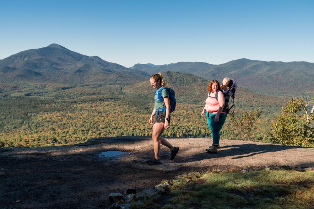Two women and a baby at the summit of Mt. Van Hoevenberg in early fall overlooking the mountain range.