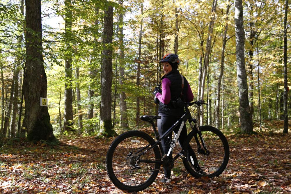 "Female smiling at the camera with a Lake Placid mountain bike rental surrounded by fallen leaves