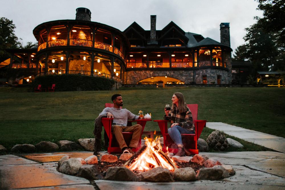 A man and woman enjoy a glass of wine at a fire pit on resort property.