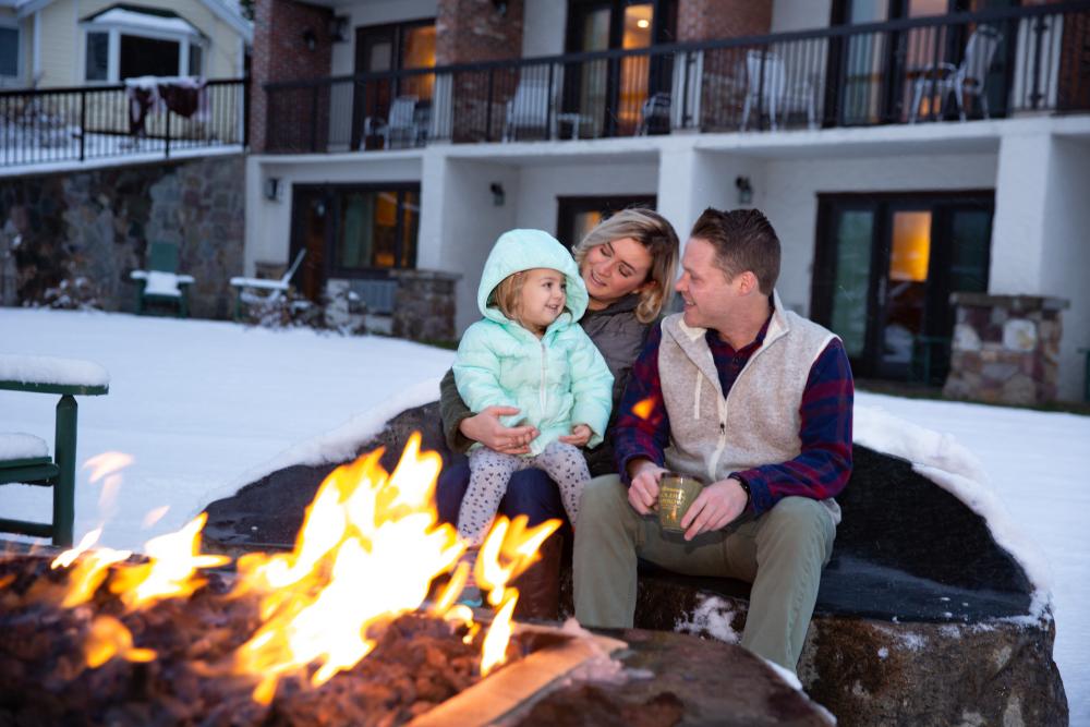 A couple with their child in front of a fire outdoors.