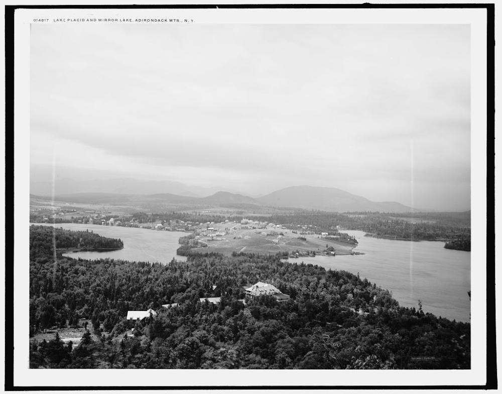 A vintage black and white aerial photo of forest, lakes, and a small village from the early 20th century.