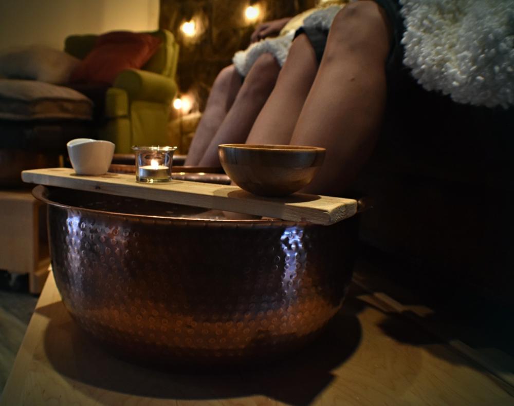 Two people sit with their feet in hammered copper bowls for a foot treatment.
