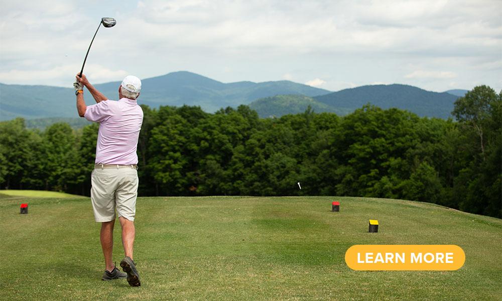 A golfer tees off toward the Adirondack Mountains.