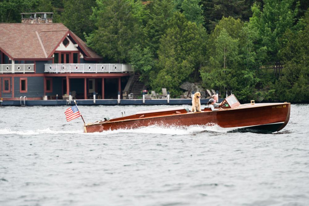 A sleek, classic wooden motor boat on Lake Placid lake with elaborate boathouse in the background.