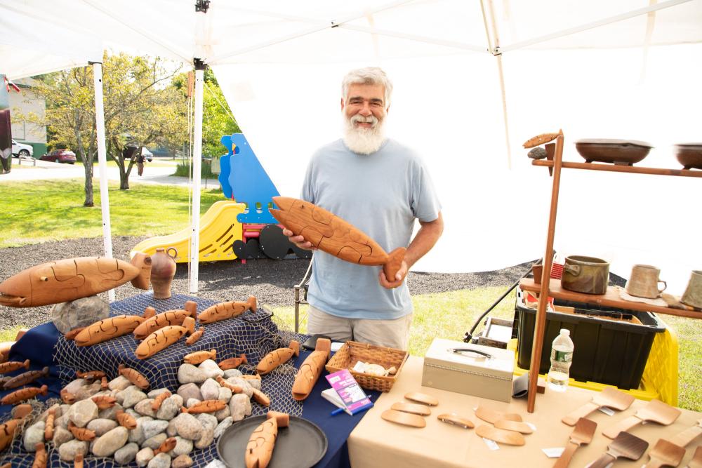 A local craftsman holds up a wooden fish at the farmers market.