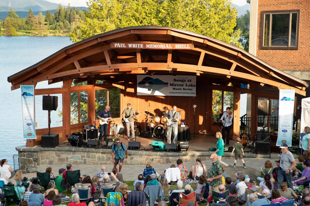 A band of four men plays in the bandshell next to Mirror Lake with an audience.