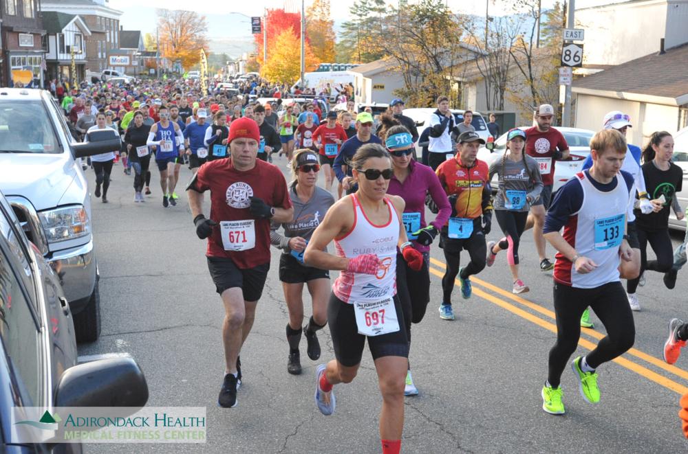 Runners race down a road aligned with fall foliage.