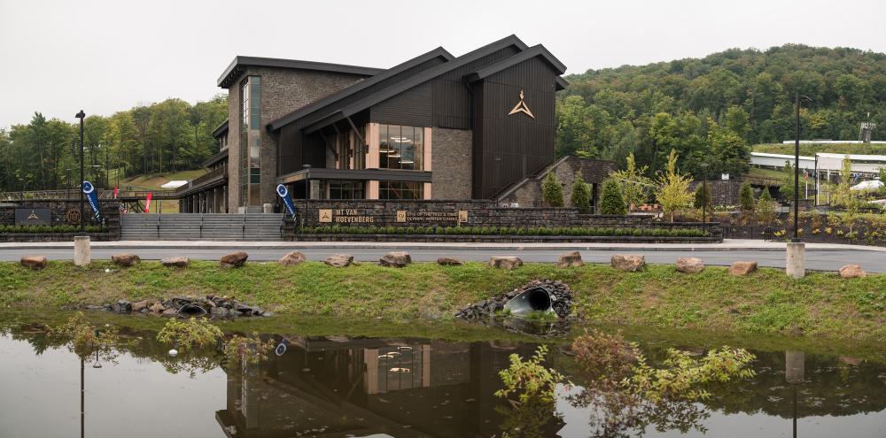 The new, modern Mountain Pass Lodge is classic Adirondack rustic design with a modern twist. It is surrounded by trees and hills.