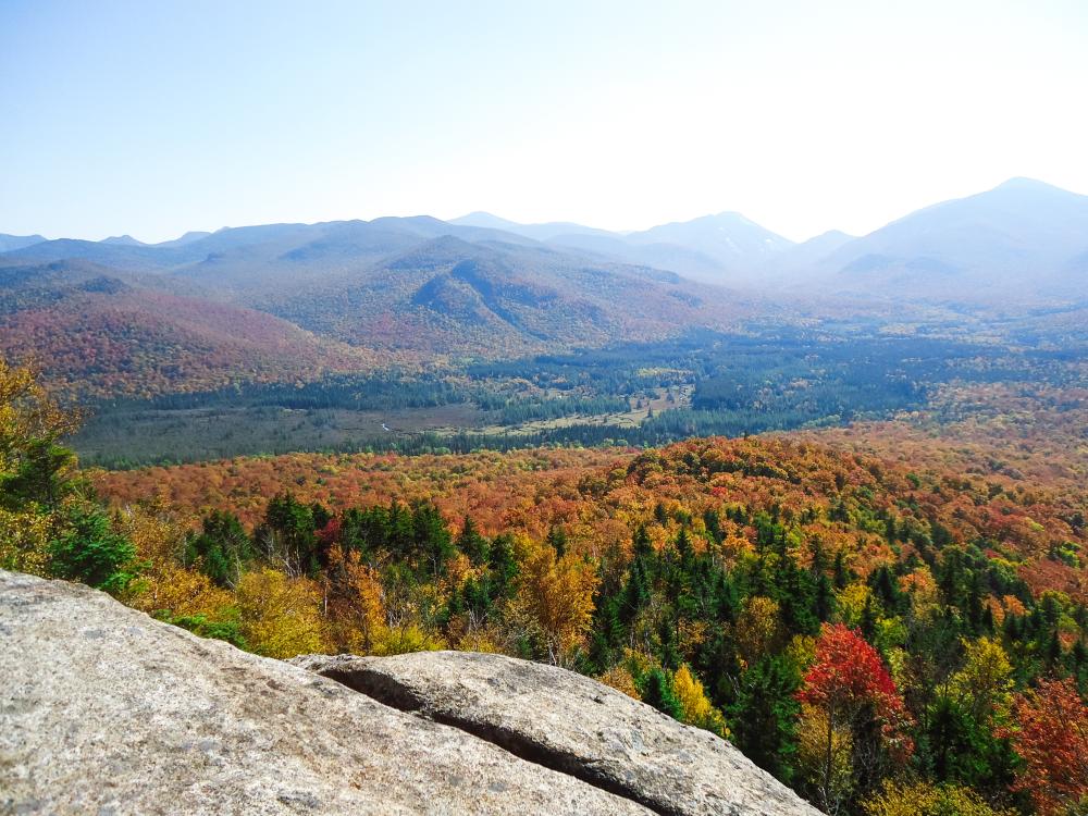 Fall view from the summit of Mount Van Hoevenberg. The High Peaks are covered in vibrant, colorful foliage.