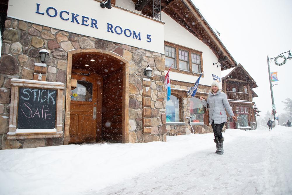 As the snow flies, a woman in a white coat walks by Locker Room 5.