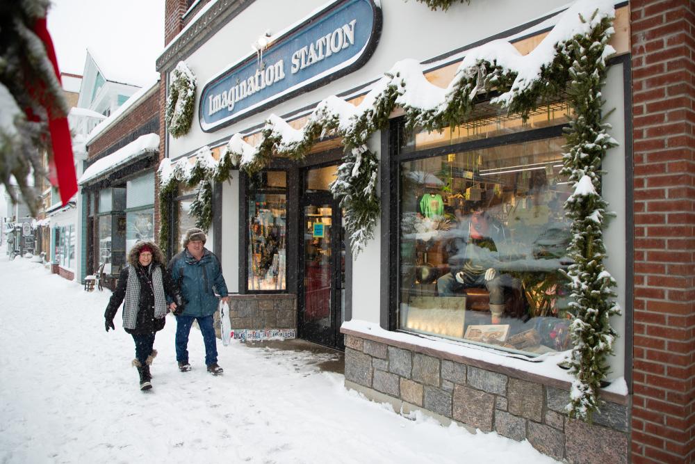 A man and woman walking together down a snowy Main Street sidewalk.