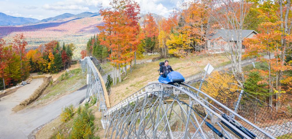 Man rides mountain roller coaster with fall foliage and mountains in background