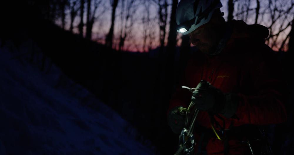 Man stands organizing ice climbing gear at dawn