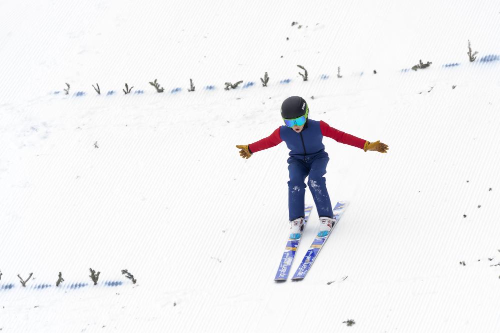 A young ski jumper landing on the snow.