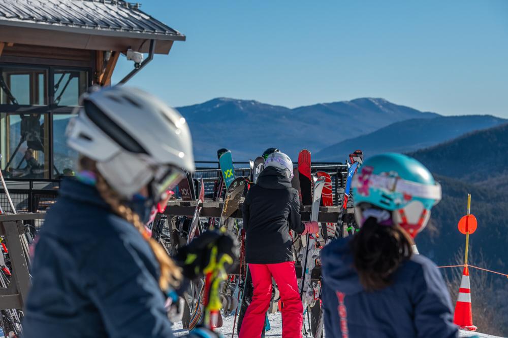 Skiers retrieve their skis from the stands outside a building.