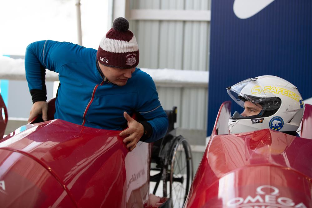 Two adaptive bobsled athletes chat while preparing for a practice run down the Lake Placid bobsled track