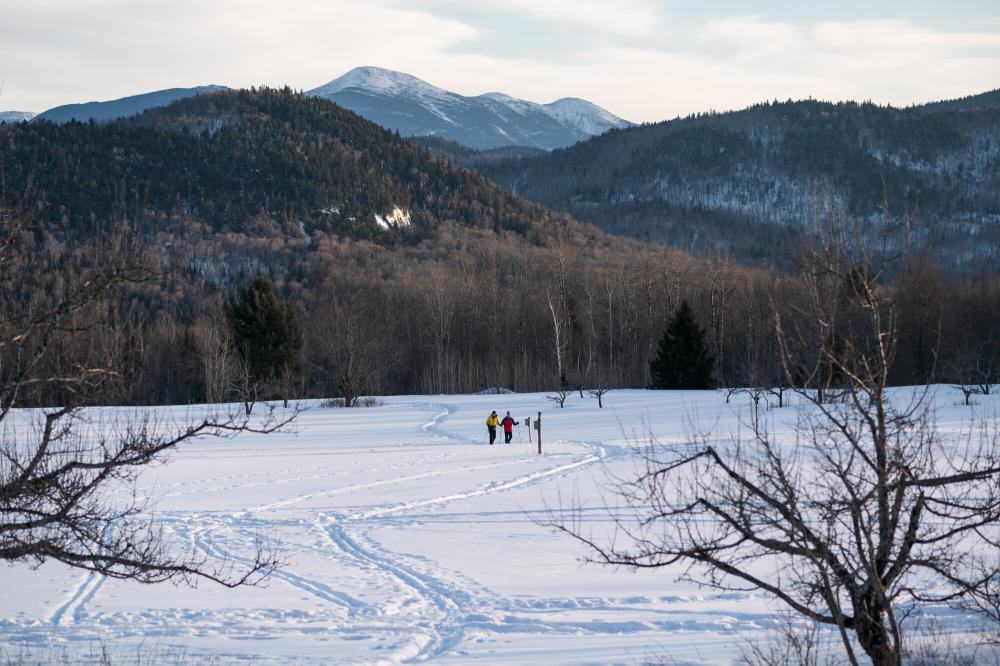 Two distant people in the snowy open field at Heaven Hill with the High Peaks rising in the background.