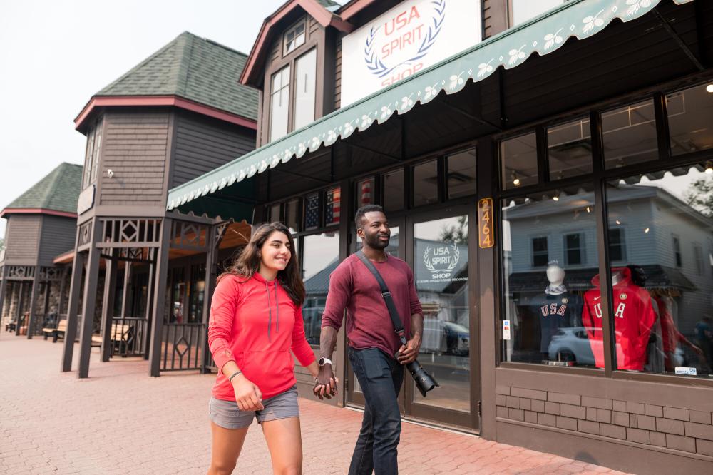 A man and woman holding hands walk past a store on a brick sidewalk.