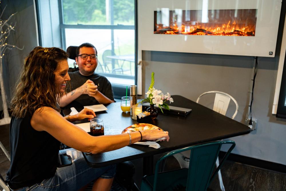 A woman and a man in a wheelchair eating pizza at a table.