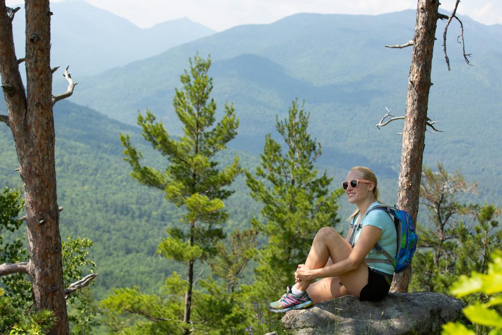 A woman sitting on a rock on top of a mountain overlooking the peaks in the distance.